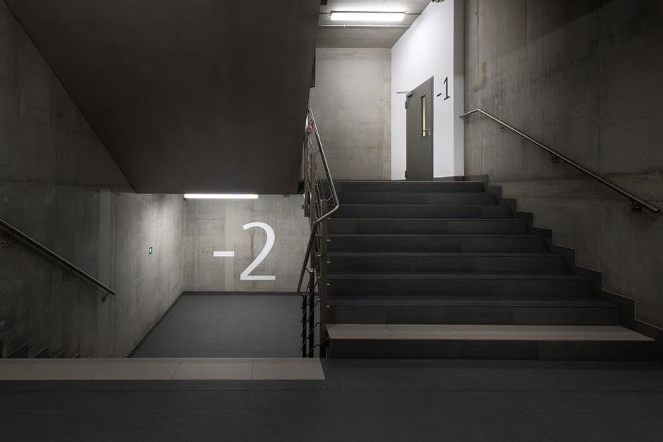 A minimalist underground stairwell with concrete walls and clear signage.