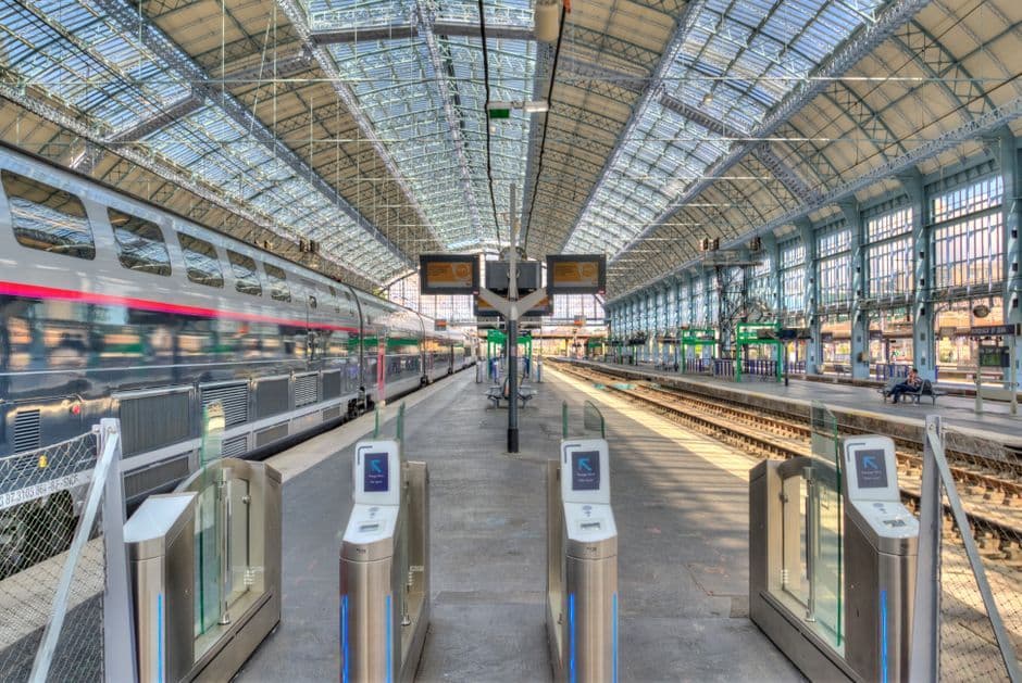 Wide-angle view of a modern train station platform with a parked train under a glass roof.